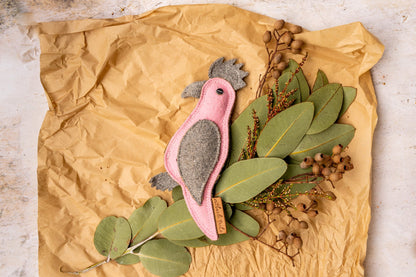 Eco friendly dog toy Gertie Galah by outback tails laying on a bed of Australian native plants on brown wrapping paper