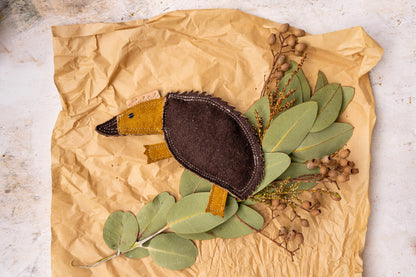 Eco friendly dog toy Ed the Echidna by outback tails laying on a bed of Australian native plants on brown wrapping paper